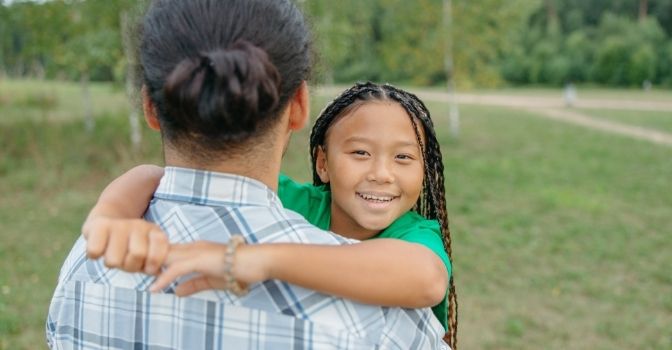 A girl is being carried by her dad and smiling into the camera.