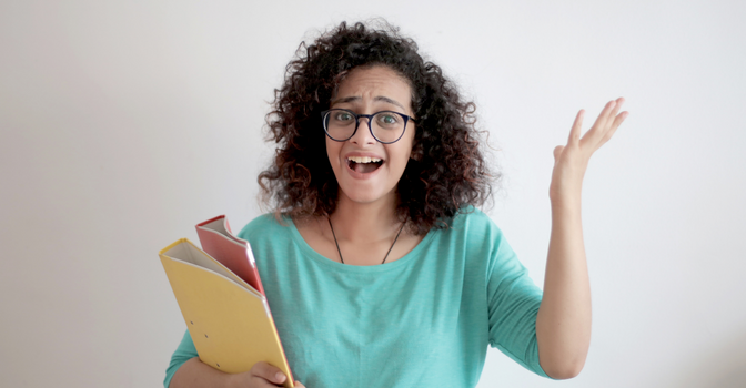 A woman throws one hand in the air while holding on to some folders.