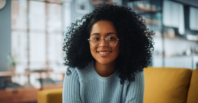 Person with glasses smiling at the camera with yellow couch in background