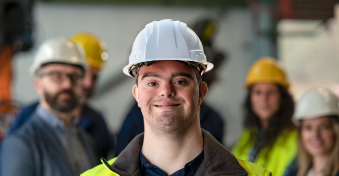 Man with disability smiling at the camera wearing a hard hat and high visibility vest.