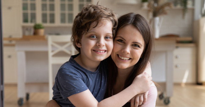 Young mother embracing preschool son, sitting on a couch at home
