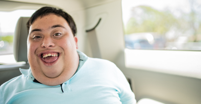 young man sitting in the back of a car, smiling at the camera wearing a light blue polo.