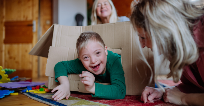 Boy with Down syndrome with his mother and grandmother playing with box together at home.