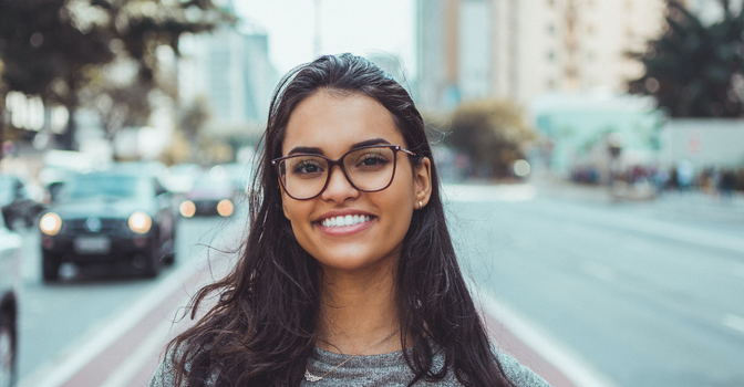 A person with glasses stands outside and smiles at the camera