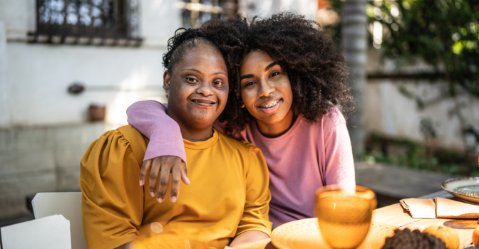 Two sisters embracing at a dinner table.