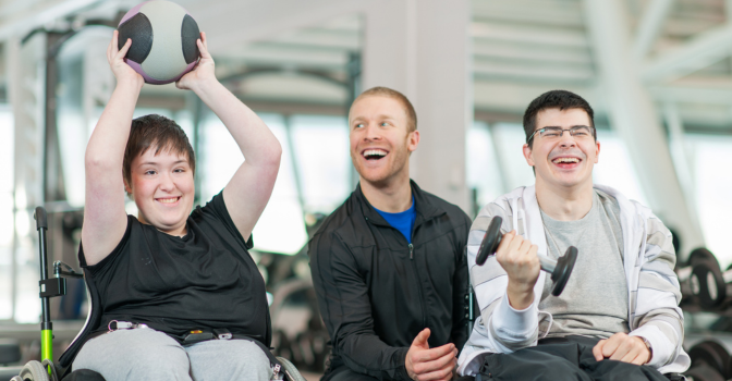 Two people with disability lifting weights in a gym with a trainer assisting them.