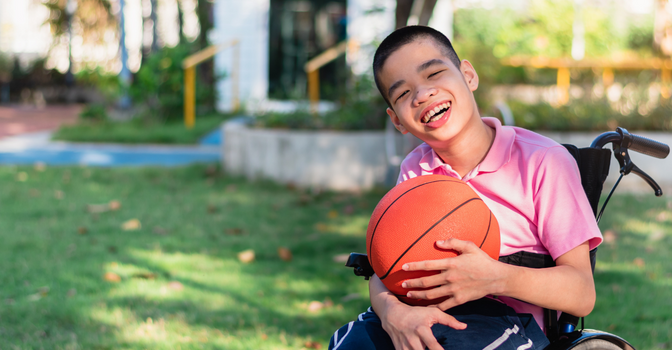 young person with disability, smiling at the camera, holding a basketball
