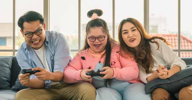 Daughter with disability playing video game on couch with parents.