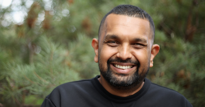 Dr Dinesh Palipana smiling at the camera with foliage behind him.