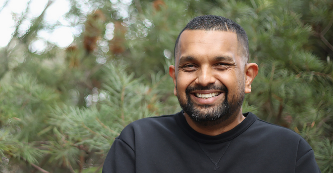 Dr Dinesh Palipana smiling at the camera with foliage behind him.