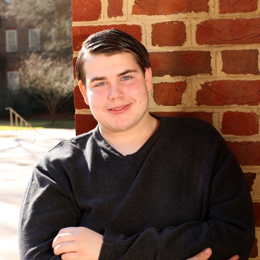 Young adult male leaning against a brickwall outside in the sunshine