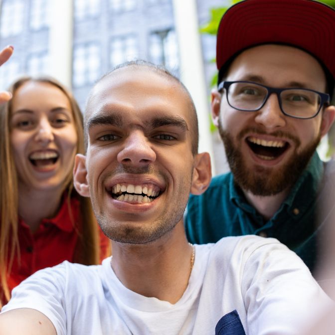 Man holding camera to take a selfie of himself and a man and a woman who are standing behind him smiling