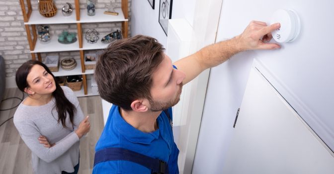 Man on ladder testing a wall mounted smoke detector