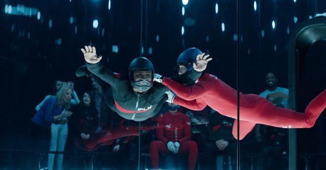Man with an iFly suit on, floating inside the indoor skydiving tunnel with an instructor