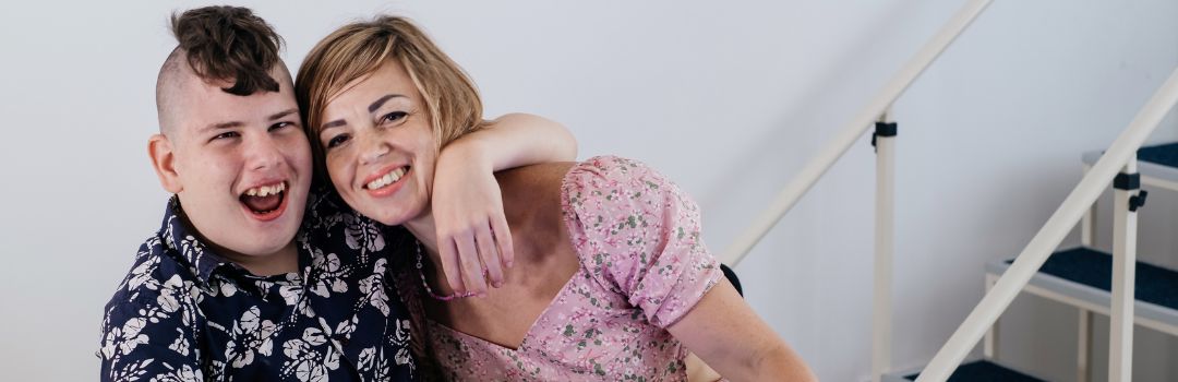 Teenage boy smiling joyfully and embracing a woman who's smiling at the camera