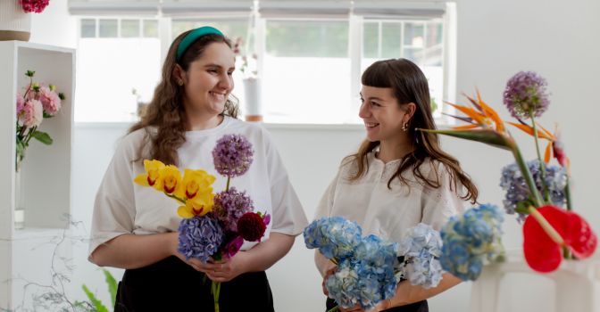 Two women smiling at each other arranging brightly coloured flowers