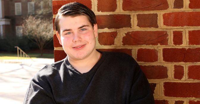 Young adult male leaning against a brickwall outside in the sunshine