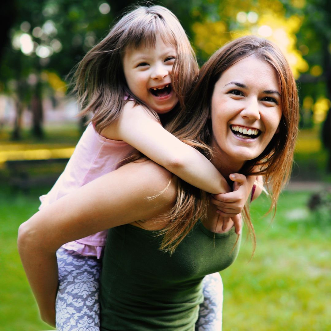 Woman smiling with a young girl on her back also laughing
