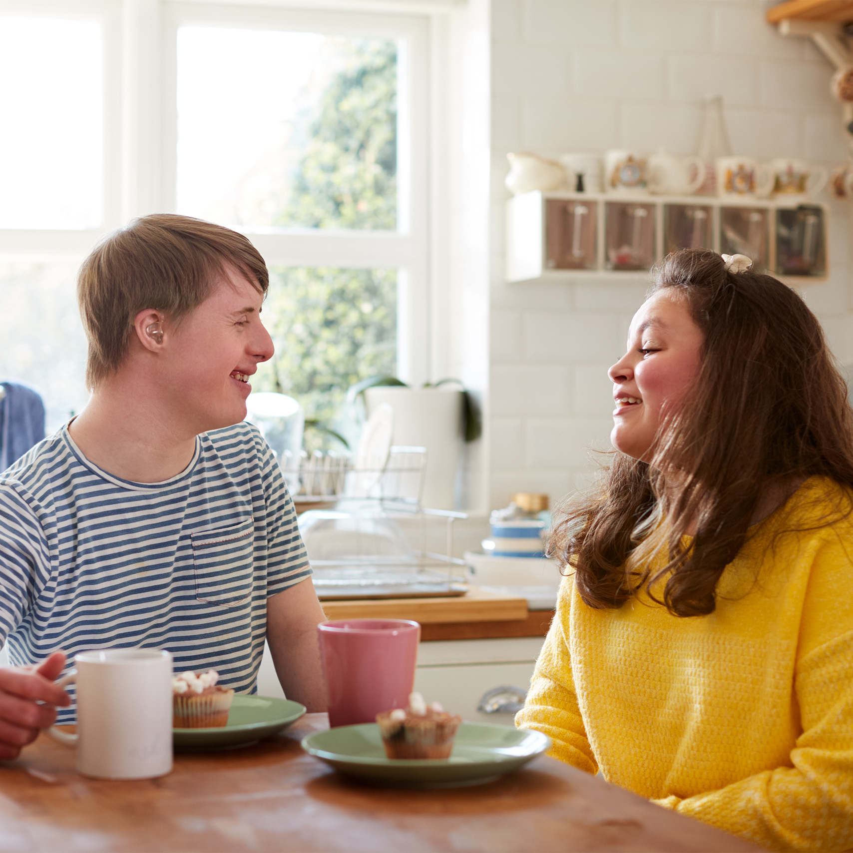 Man with a hearing aid smiles at a woman as they sit in a kitchen