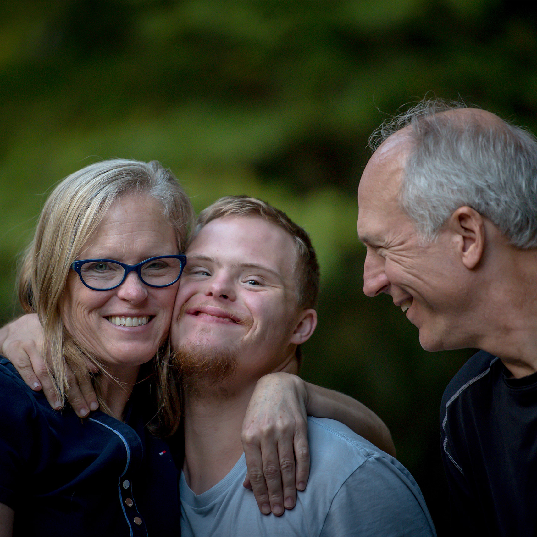 mother hugs son while father watches and smiles