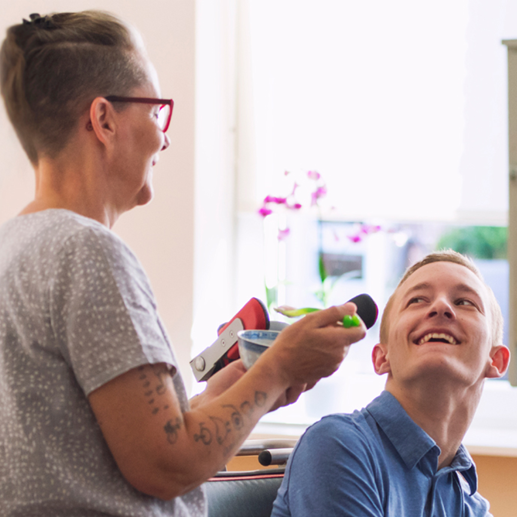 Woman is feeding a young man in a wheelchair