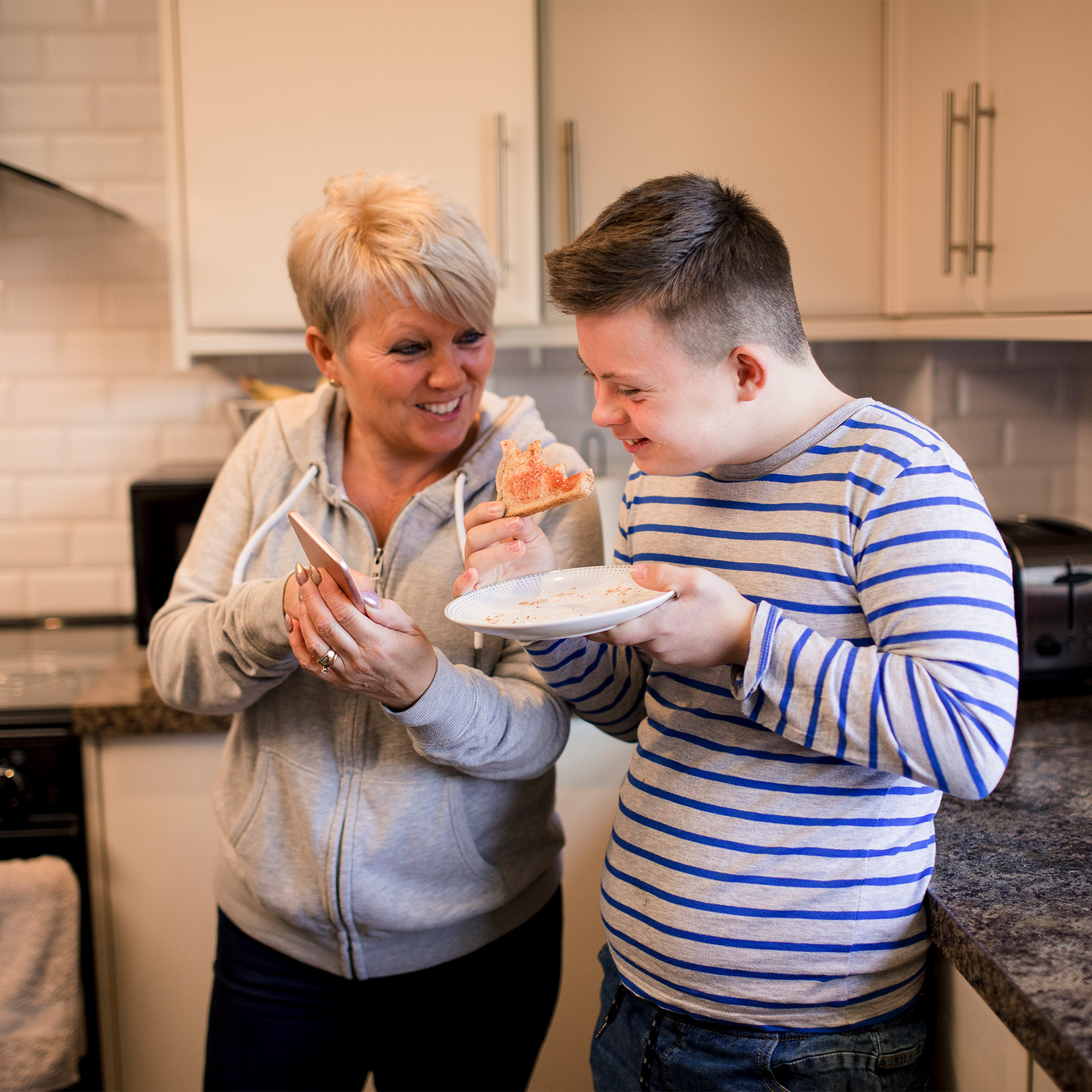 Mother smiles at teenage son as he eats toast