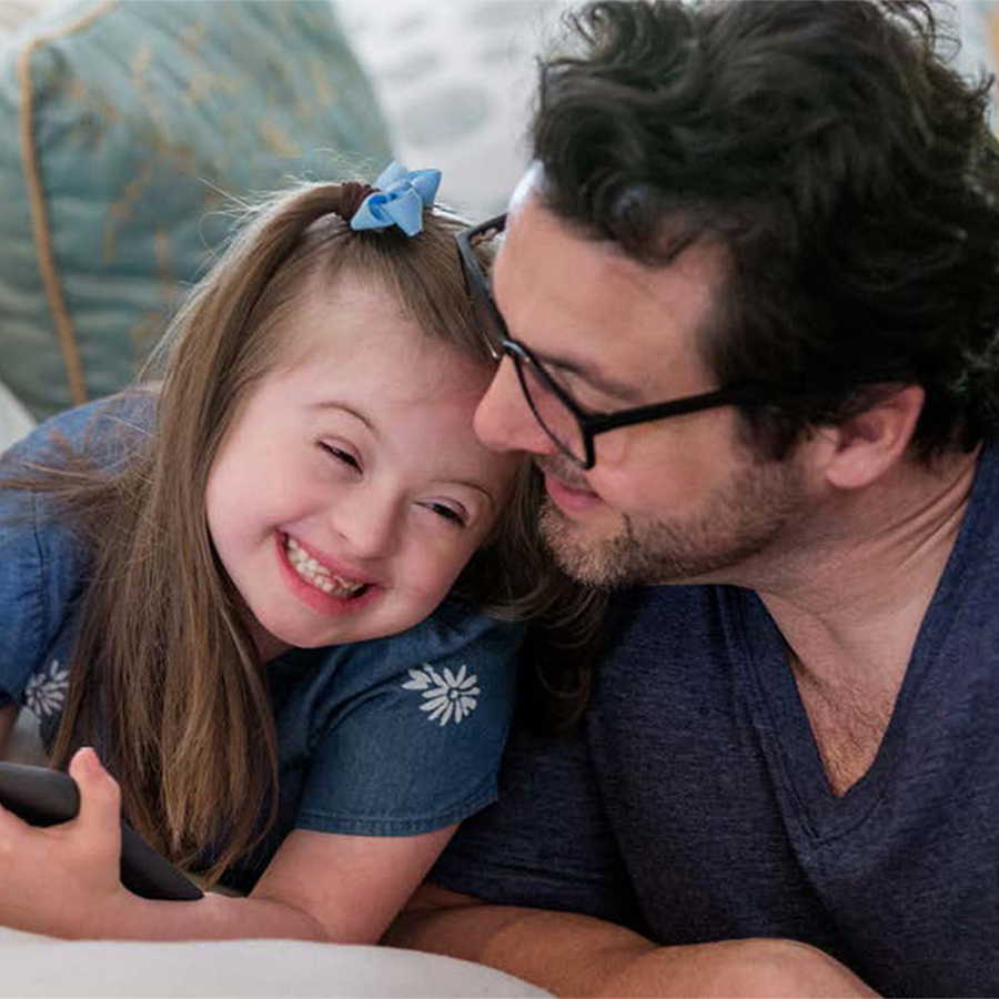 Father and daughter smile as they lean together on a couch