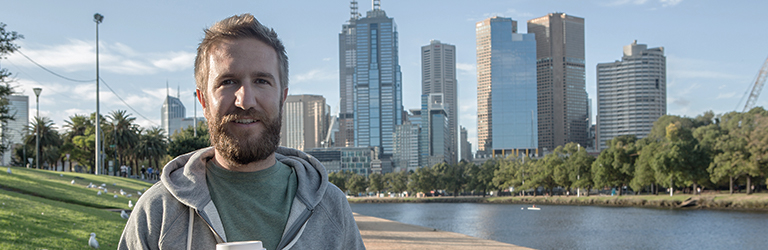 Bearded man wearing a tracksuit standing next to the Brisbane River