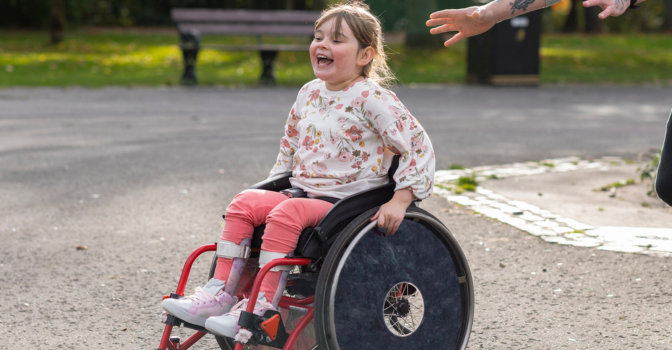 A low angle close-up of a father and his young daughter who is a wheelchair user playing.