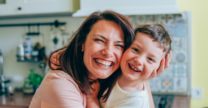 Mother and son embracing in a kitchen, laughing at the camera.