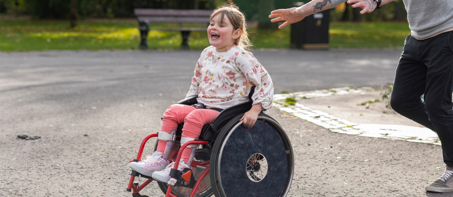 A low angle close-up of a father and his young daughter who is a wheelchair user playing.