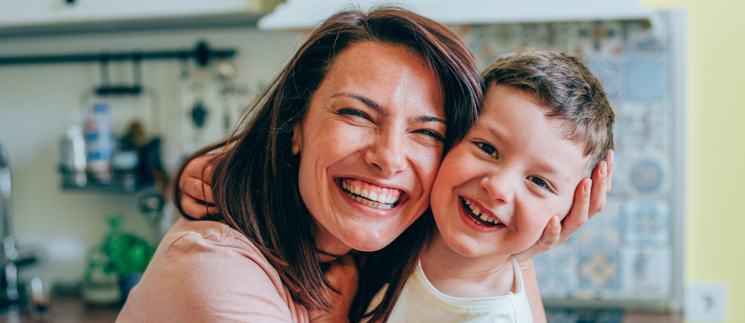 Mother and son embracing in a kitchen, laughing at the camera.