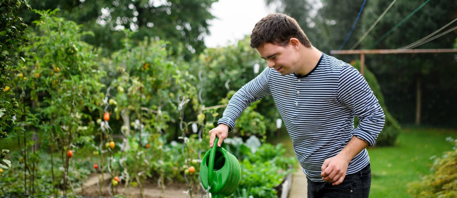 Young person with disability standing outside, watering the garden.