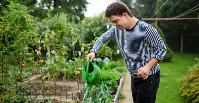 Young person with disability standing outside, watering the garden.