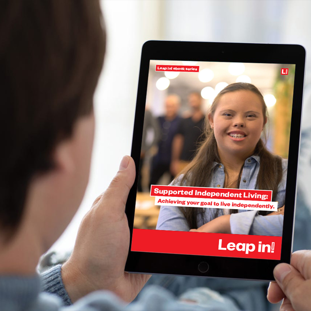 Looking over the shoulder of a boy holding an tablet with the Leap in! cover of the Supported Independant Living ebook showing on the display.