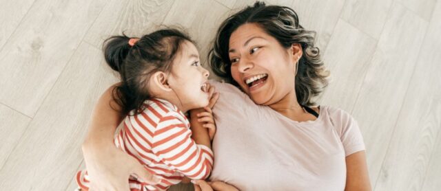 Mother embracing young daughter on the floor laughing