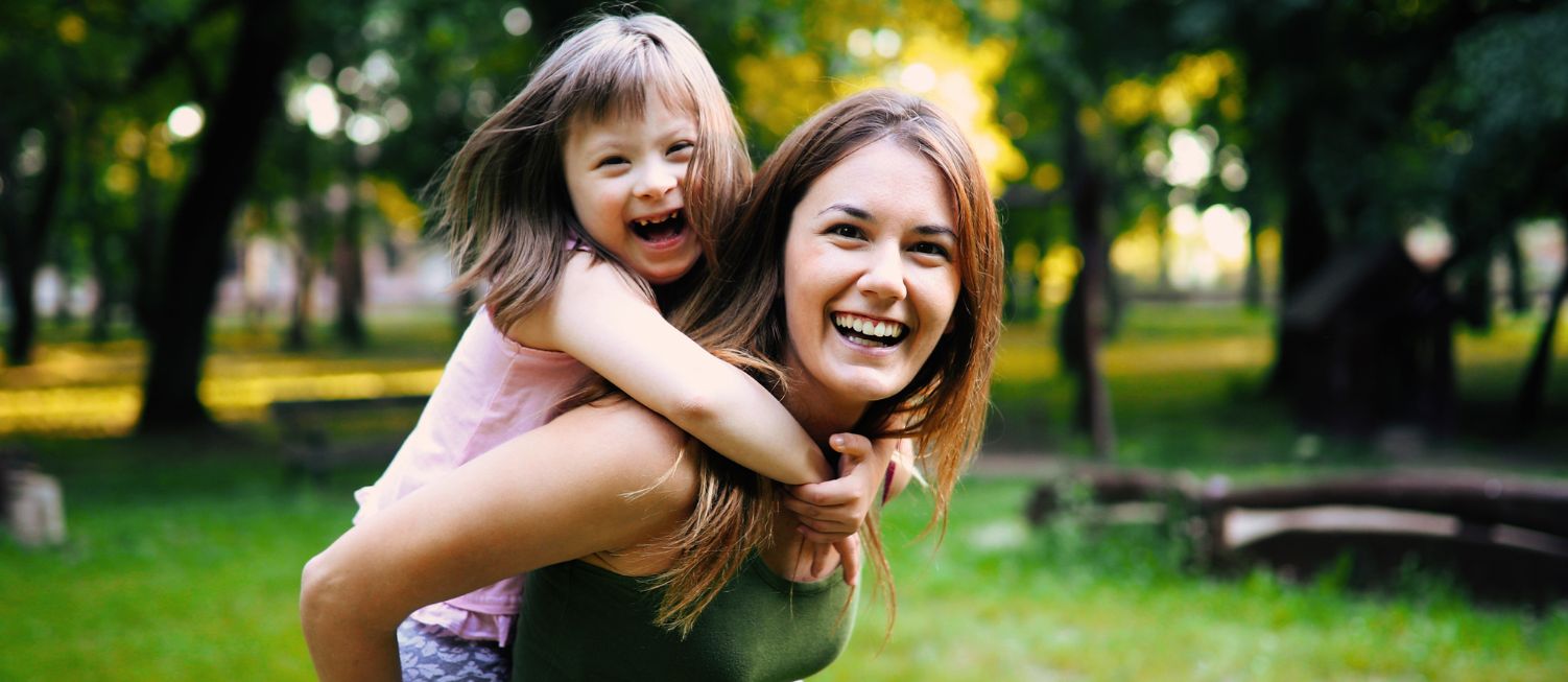 Woman smiling with a young girl on her back also laughing