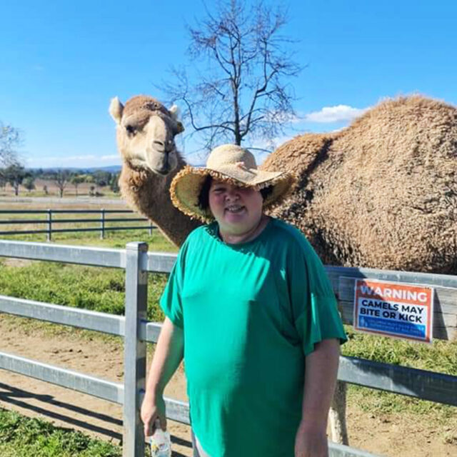 Leap in! member Lisa standing in front of a camel in its enclosure