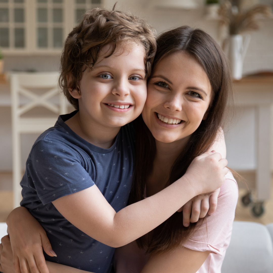 Young mother embracing preschool son, sitting on a couch at home